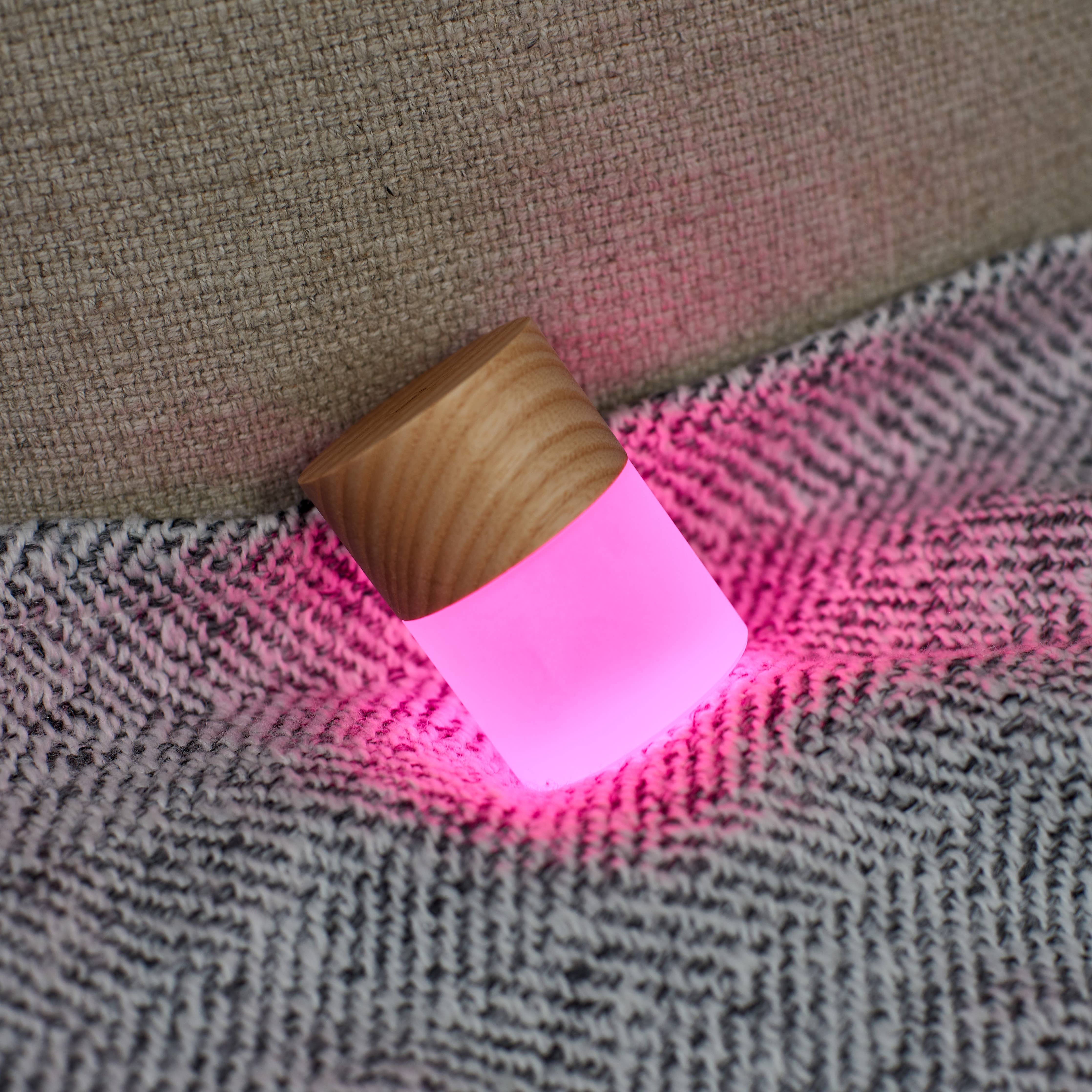 Lemelia light resting on a grey sofa cushion casting a pink glow