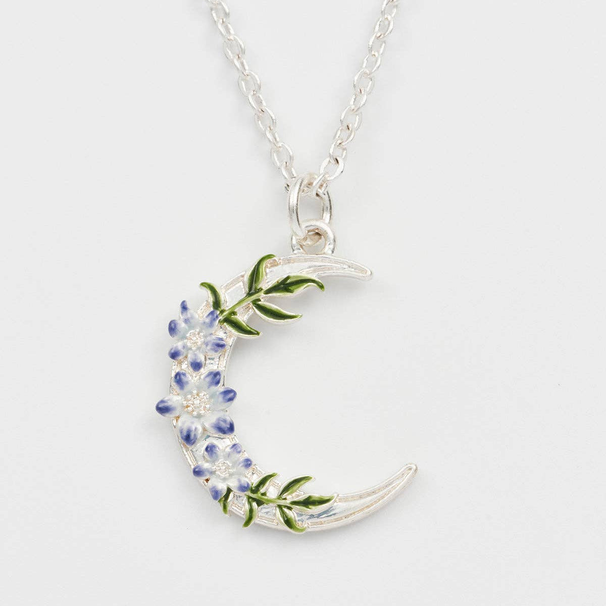 Close-up of enamel nightshade floral detail on silver crescent moon pendant