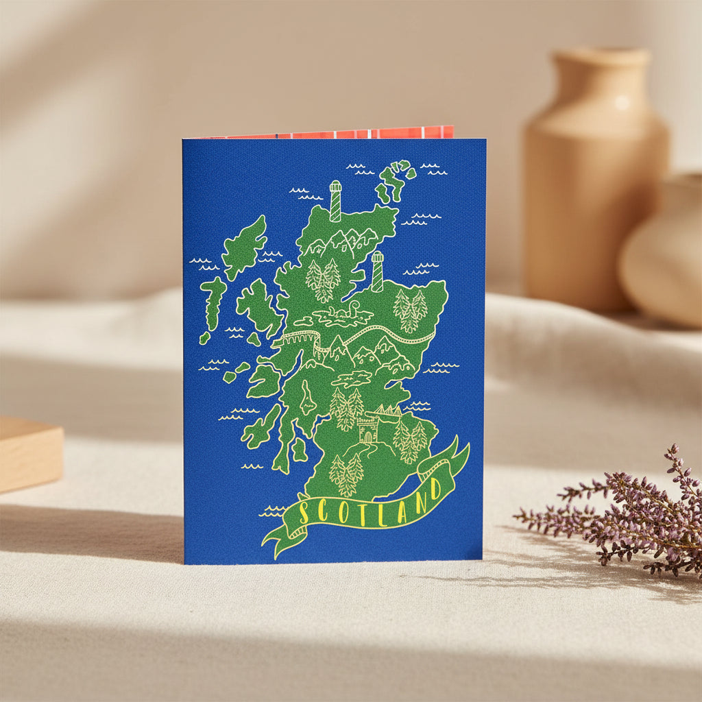A Scotland map art print or card featuring a green stylized map of Scotland on a blue background, with a red-and-white plaid pattern peeking out from behind it on a white studio background.