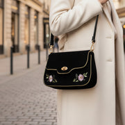 Model carrying black rose embroidered clutch bag on city street