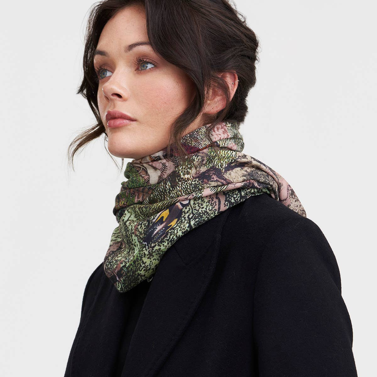 Woman wearing the woodland print scarf looped over a black coat