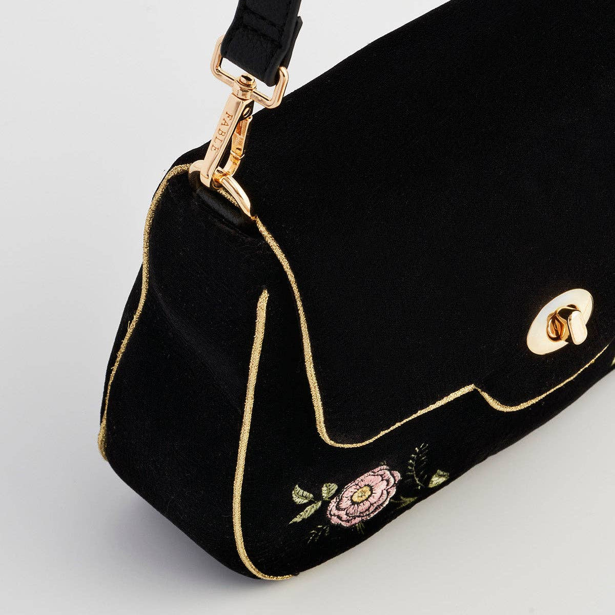 Angled detail of black clutch showing gold twist clasp and piping