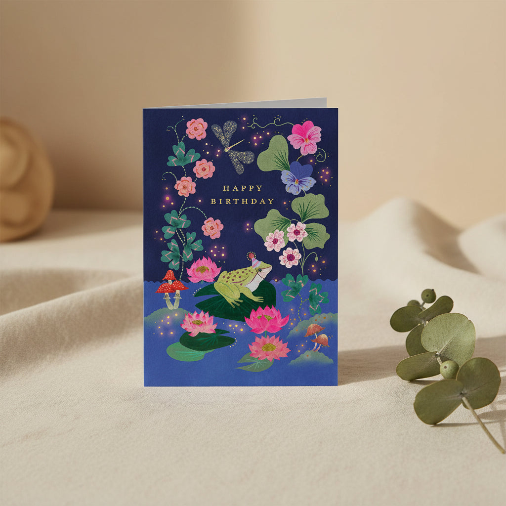 Greeting card with a frog, flowers, and 'Happy Birthday' text on a dark blue background