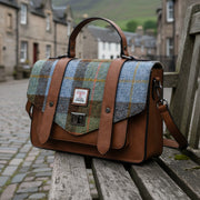 Chestnut and blue tartan Harris Tweed satchel on a bench in a cobbled street