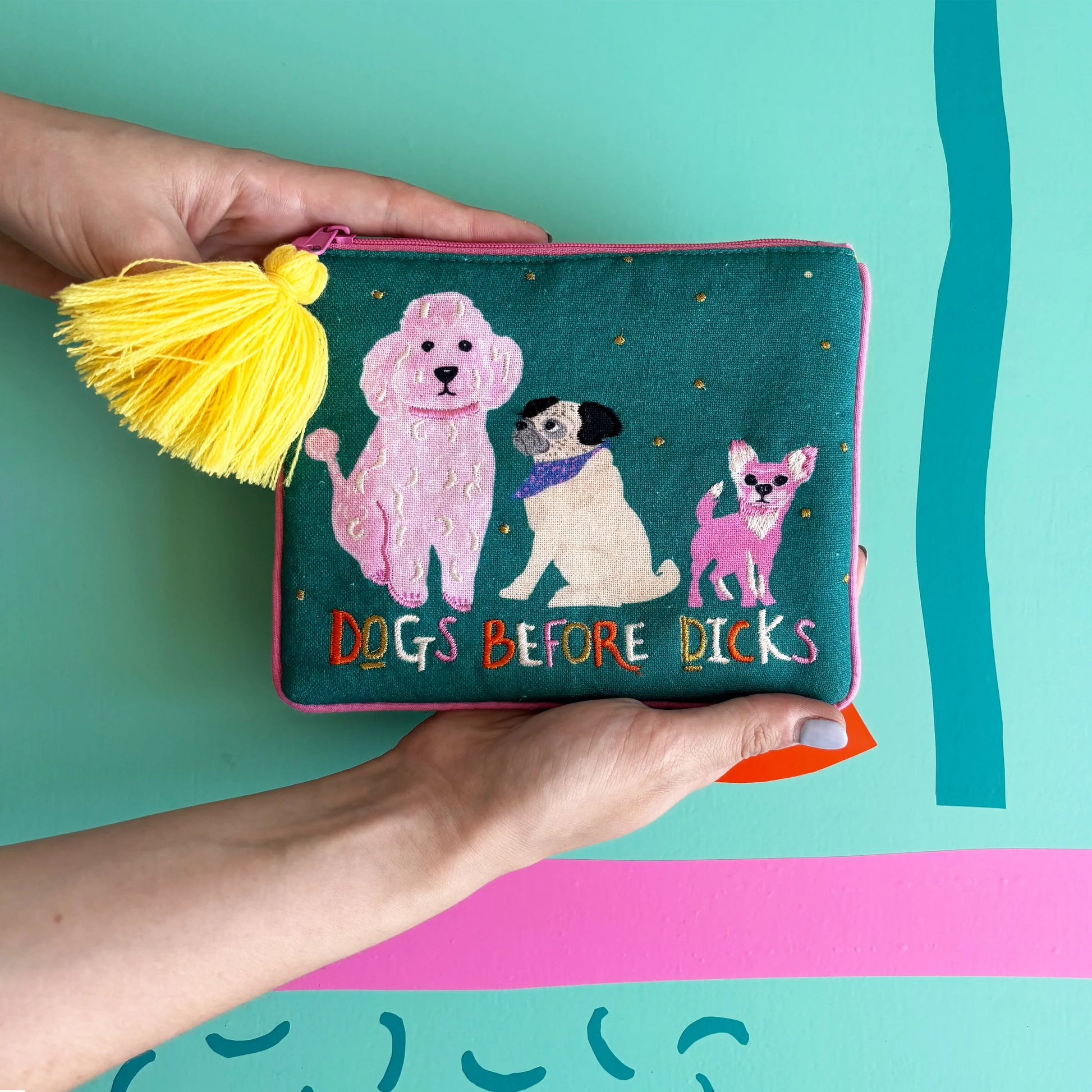 Dogs Before Dicks pouch with embroidered dogs and yellow tassel held in hands.