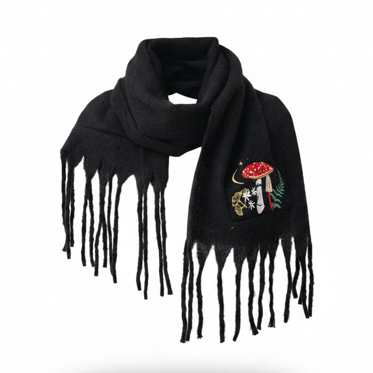 Front view of person wearing the black Forage Scarf with embroidered red toadstool and forest design, wrapped around the neck with fringe detail showing.