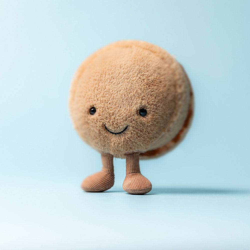 Jellycat Amuseables Mona Macaron plush posed on a pastel background, showing off its soft round shape and charming expression.