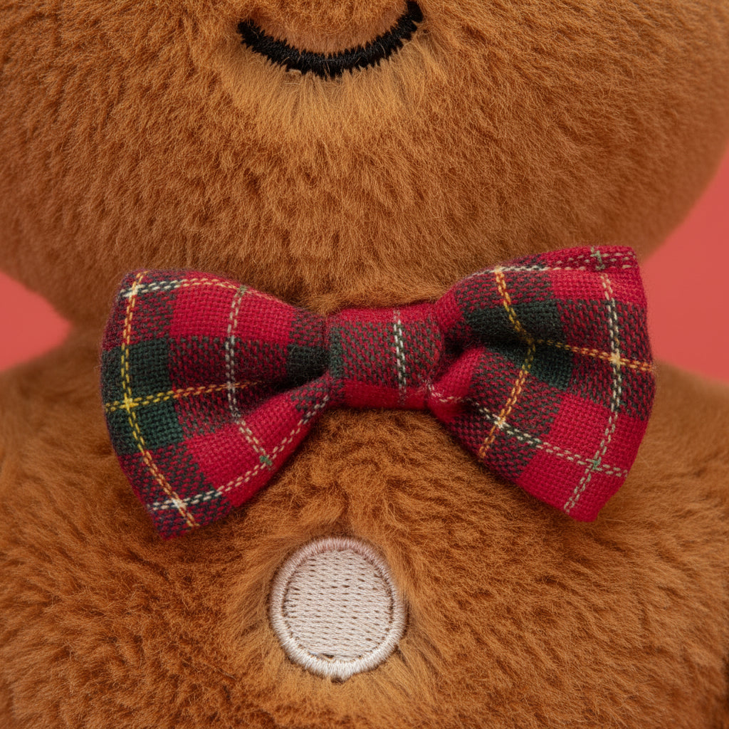 Stuffed gingerbread man toy with a plaid bow tie on a white background