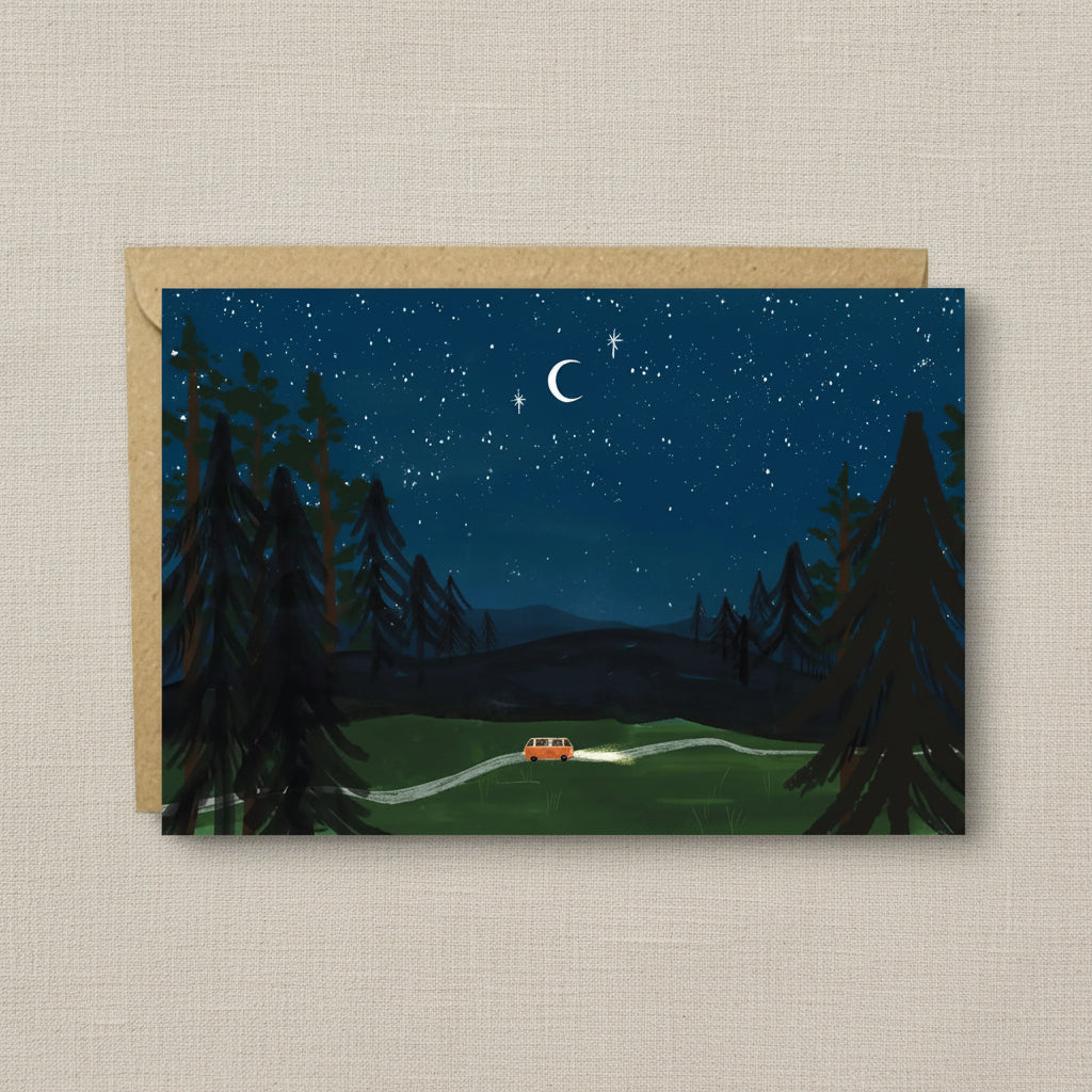 A square art print or card featuring a night forest scene with a small orange vehicle on a winding road under a starry sky and crescent moon, shown with a kraft envelope behind it on a white background.