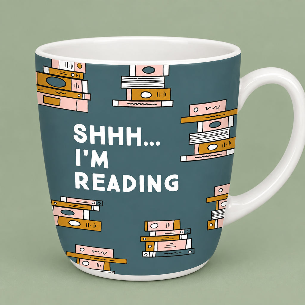 A white ceramic mug with a dark teal-blue printed background featuring illustrated stacks of books and the text 'SHHH.