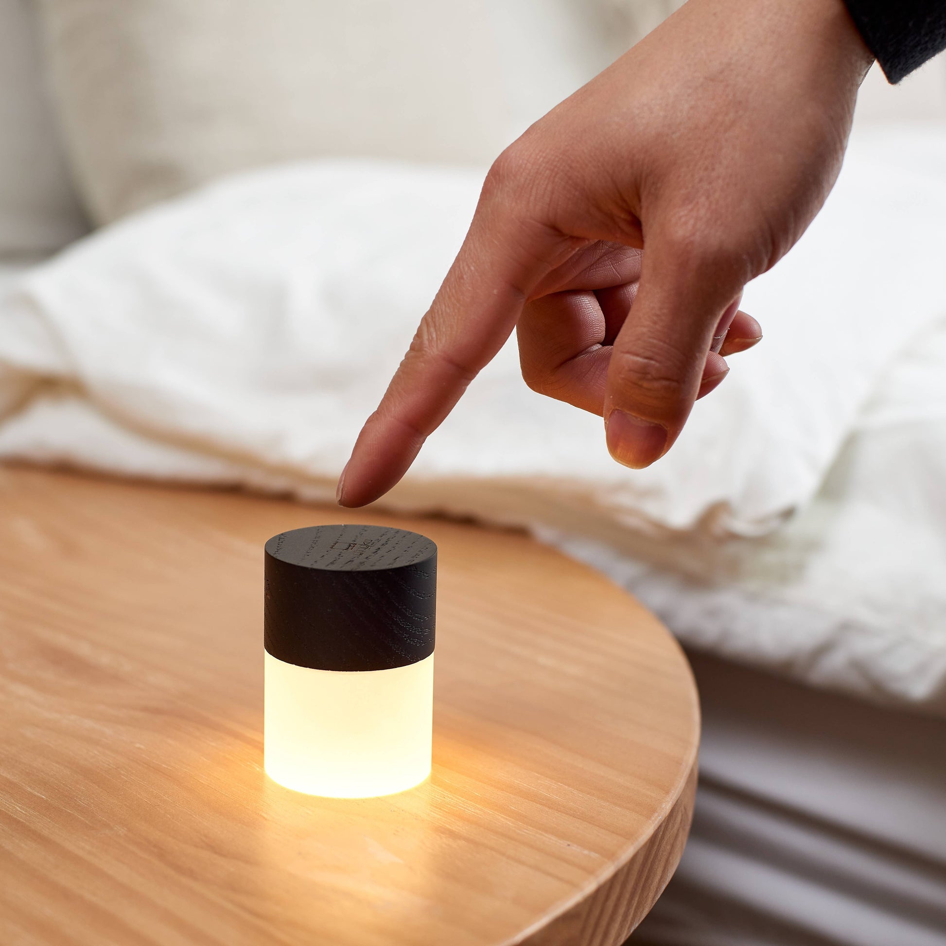 Fingertip touching the wooden top of a Lemelia light on a bedside table