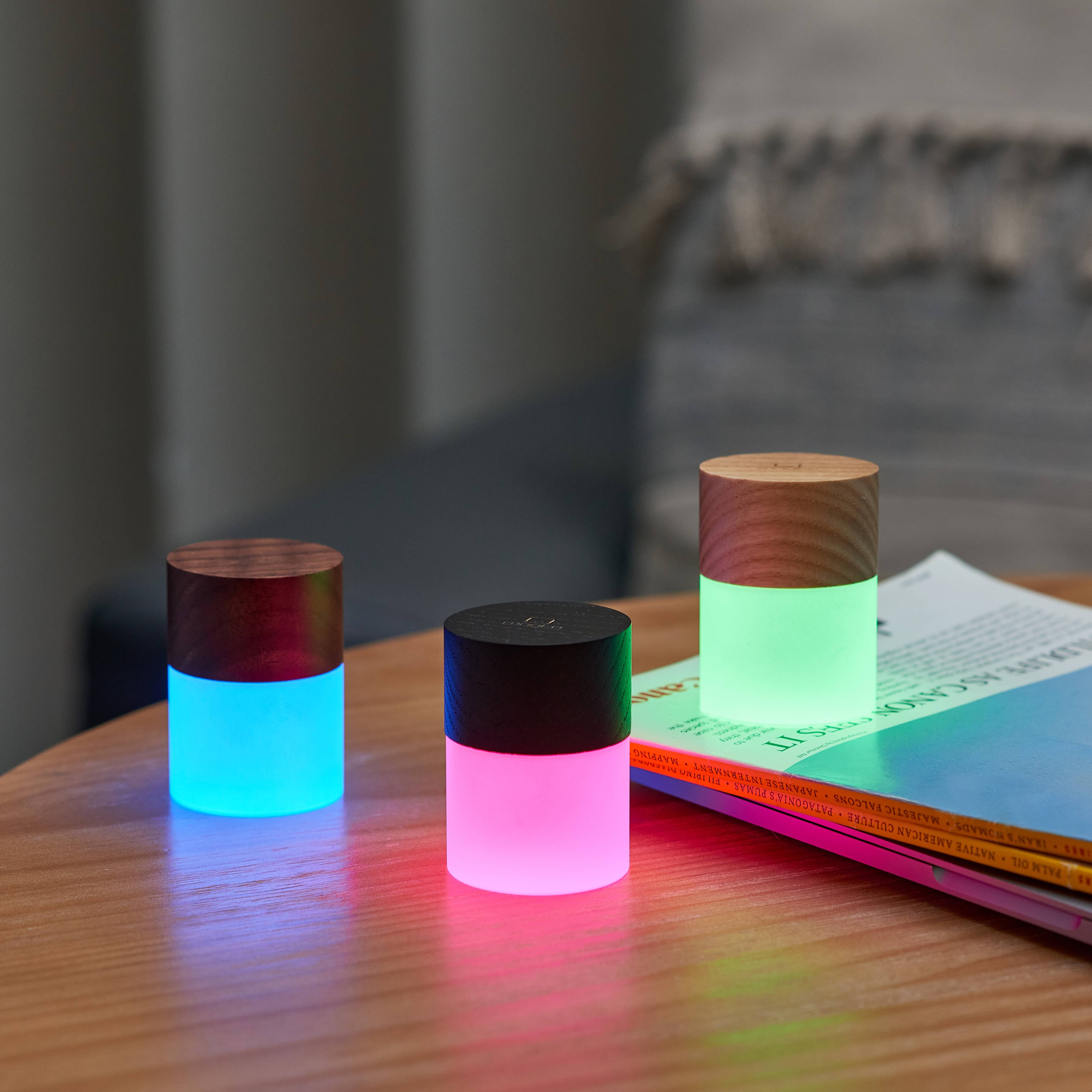 Three Lemelia lights on a wooden table glowing blue, pink and green
