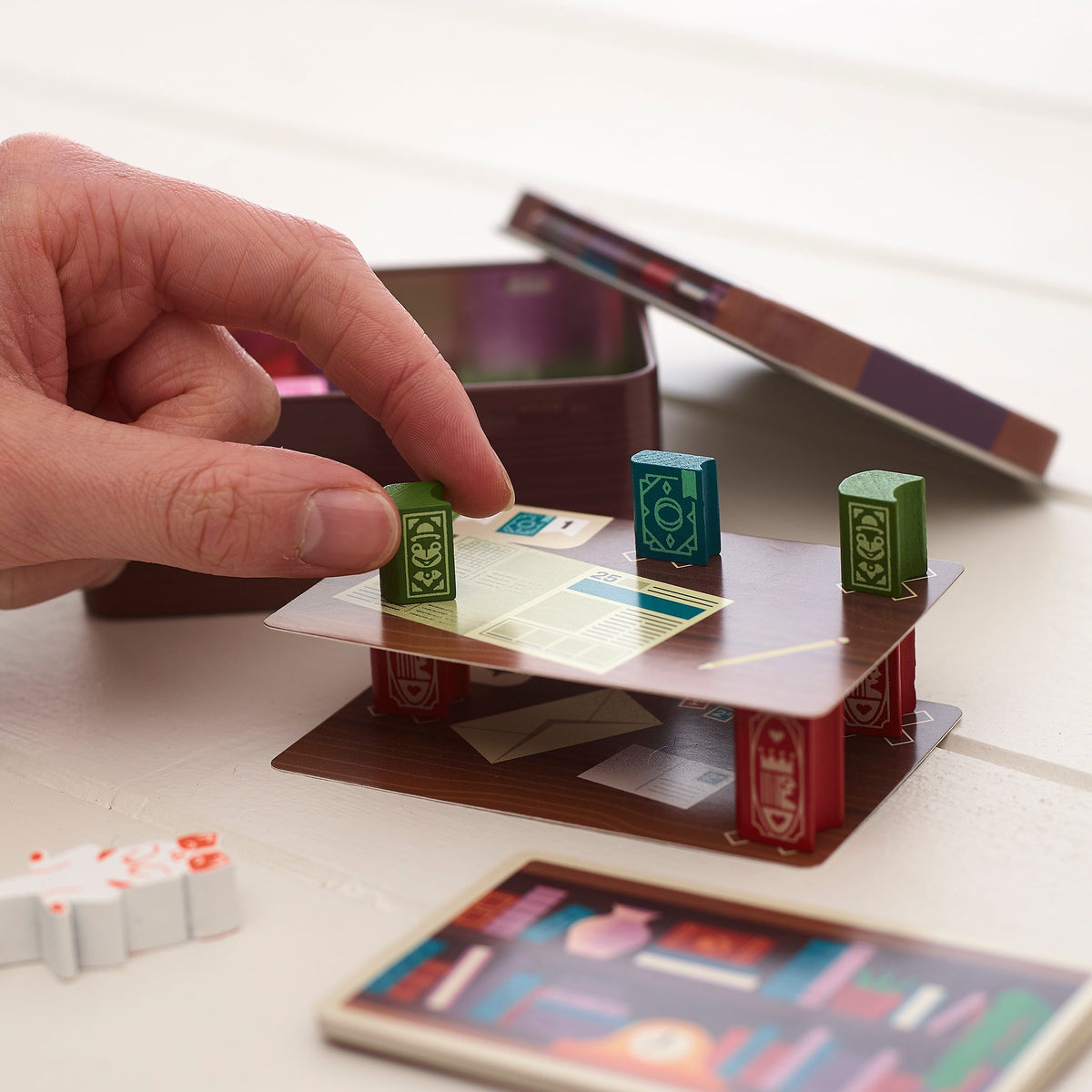 Hand placing a book onto a Bookshelf game card on a white table