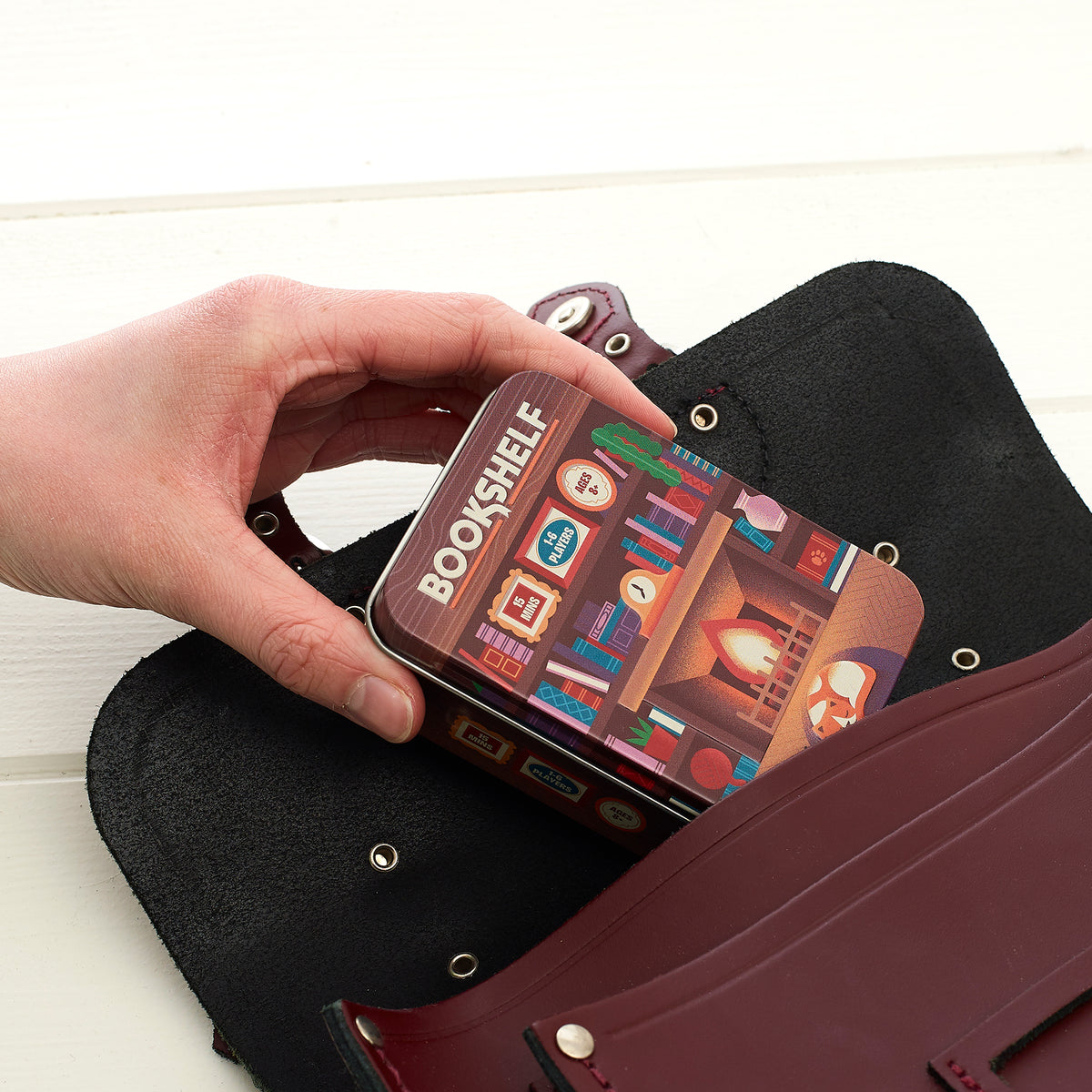 Bookshelf game tin being taken out of a leather satchel