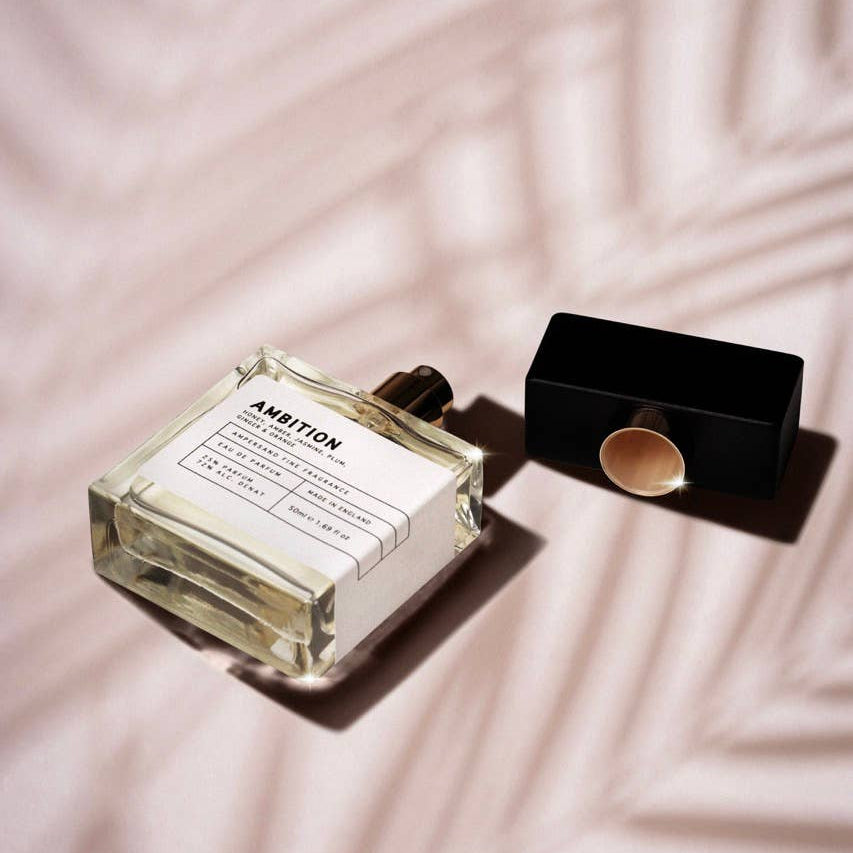 Ambition perfume bottle lying open on blush pink fabric with palm leaf shadow