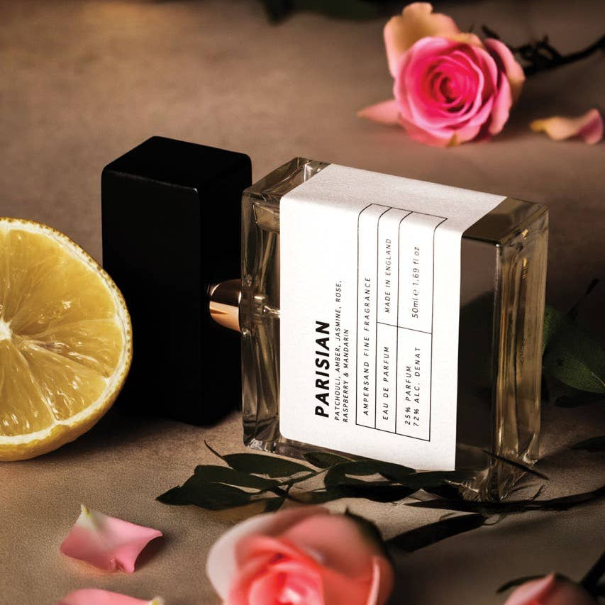 Parisian perfume bottle styled with pink roses and sliced lemon on brown surface