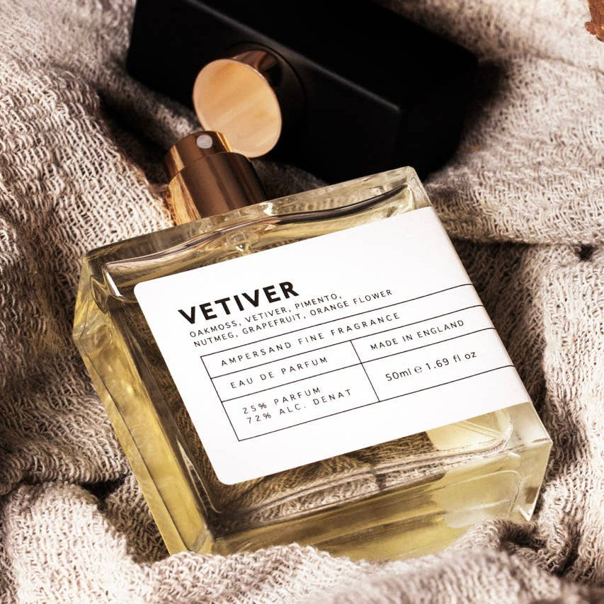 Vetiver eau de parfum resting on soft knitted fabric beside leather glasses