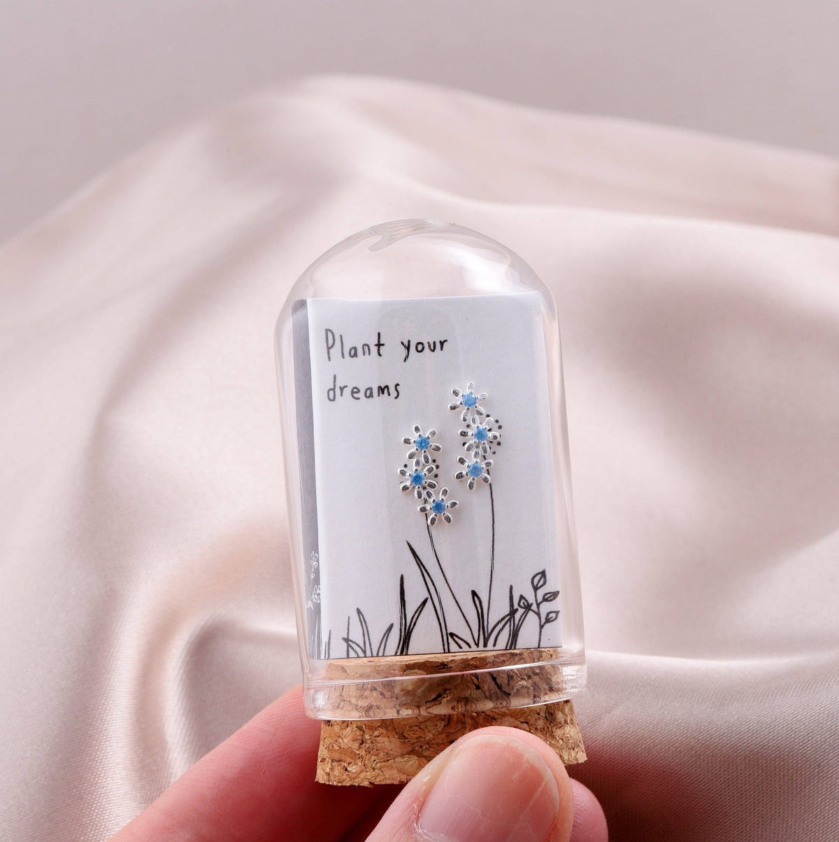 Blue crystal flower stud earrings on card inside glass terrarium held in hand