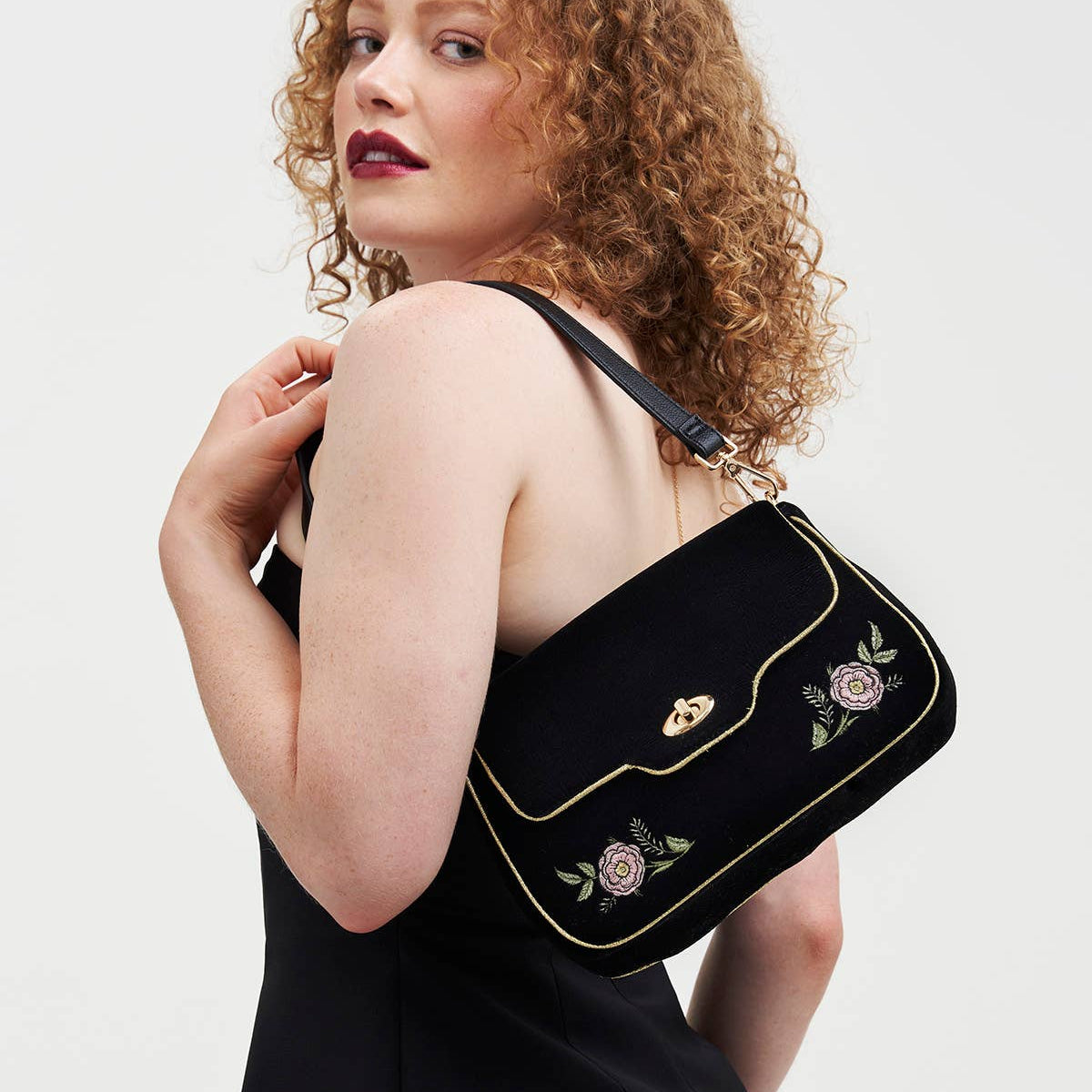 Model wearing black velvet rose embroidered clutch on shoulder