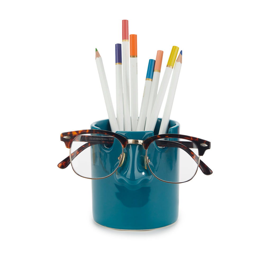Teal blue nose pen holder with coloured pencils and glasses on white