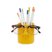 Mustard yellow nose pen holder with coloured pencils and glasses on white