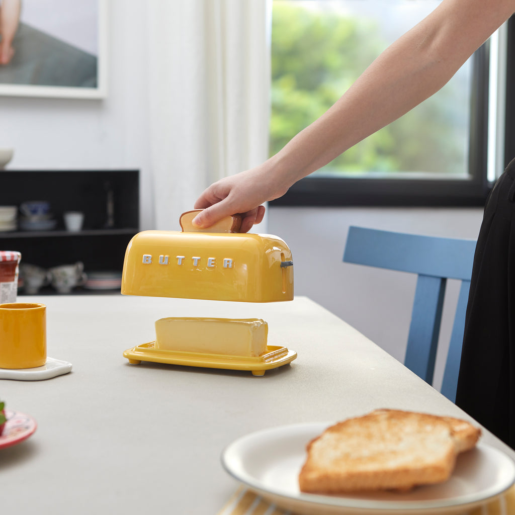 Hand lifting the toast handle of the butter dish on a bright kitchen table