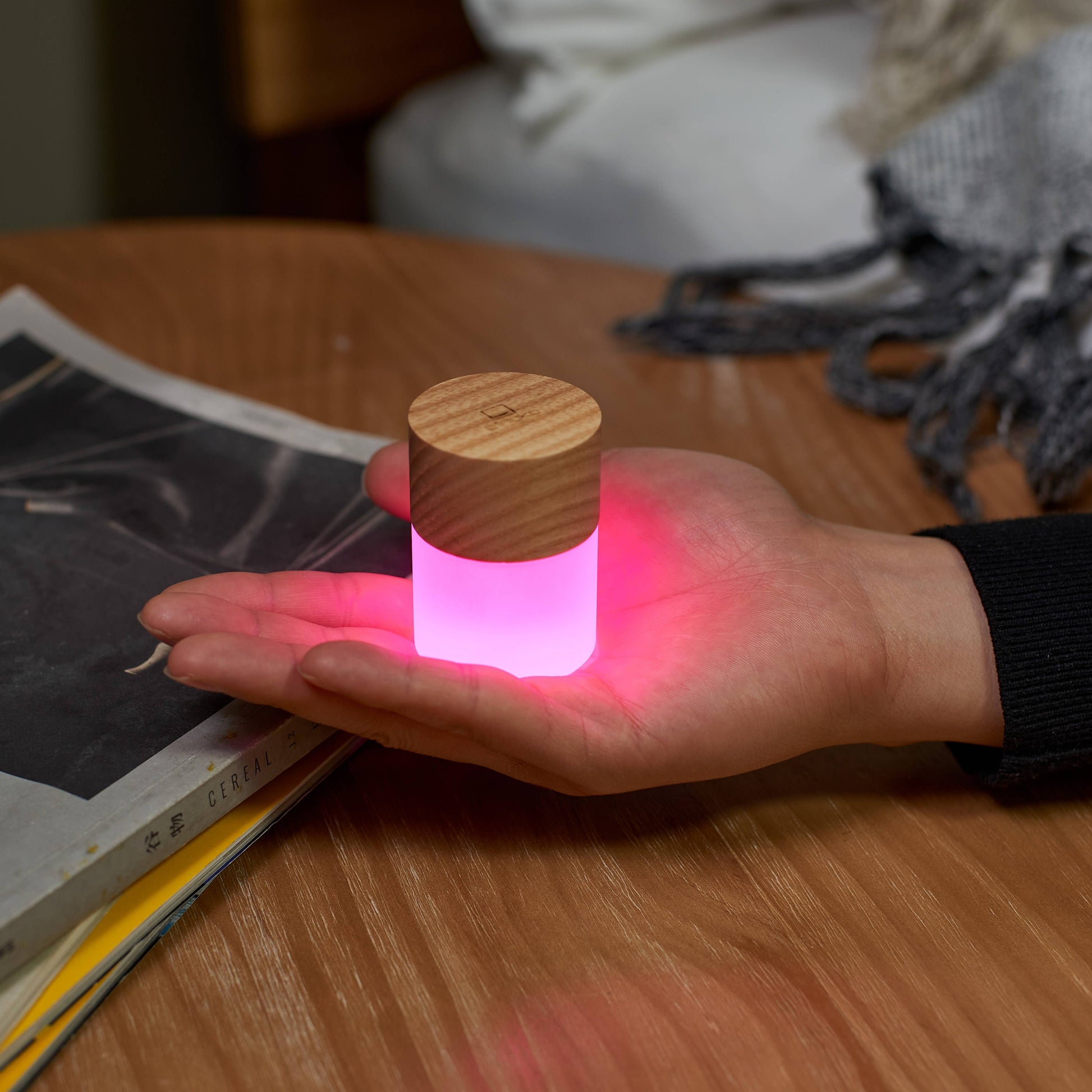 Lemelia mini light with light wood top glowing pink in a cupped hand