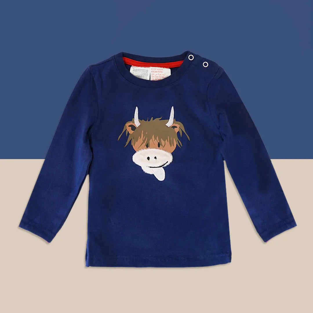 A navy blue long-sleeve baby t-shirt with a cartoon cow face graphic on the chest, displayed against a split blue and beige background.