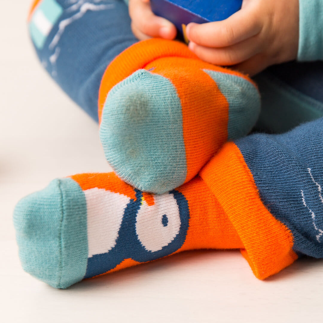 Close up of a seated child wearing the orange Kenzie the Puffin socks