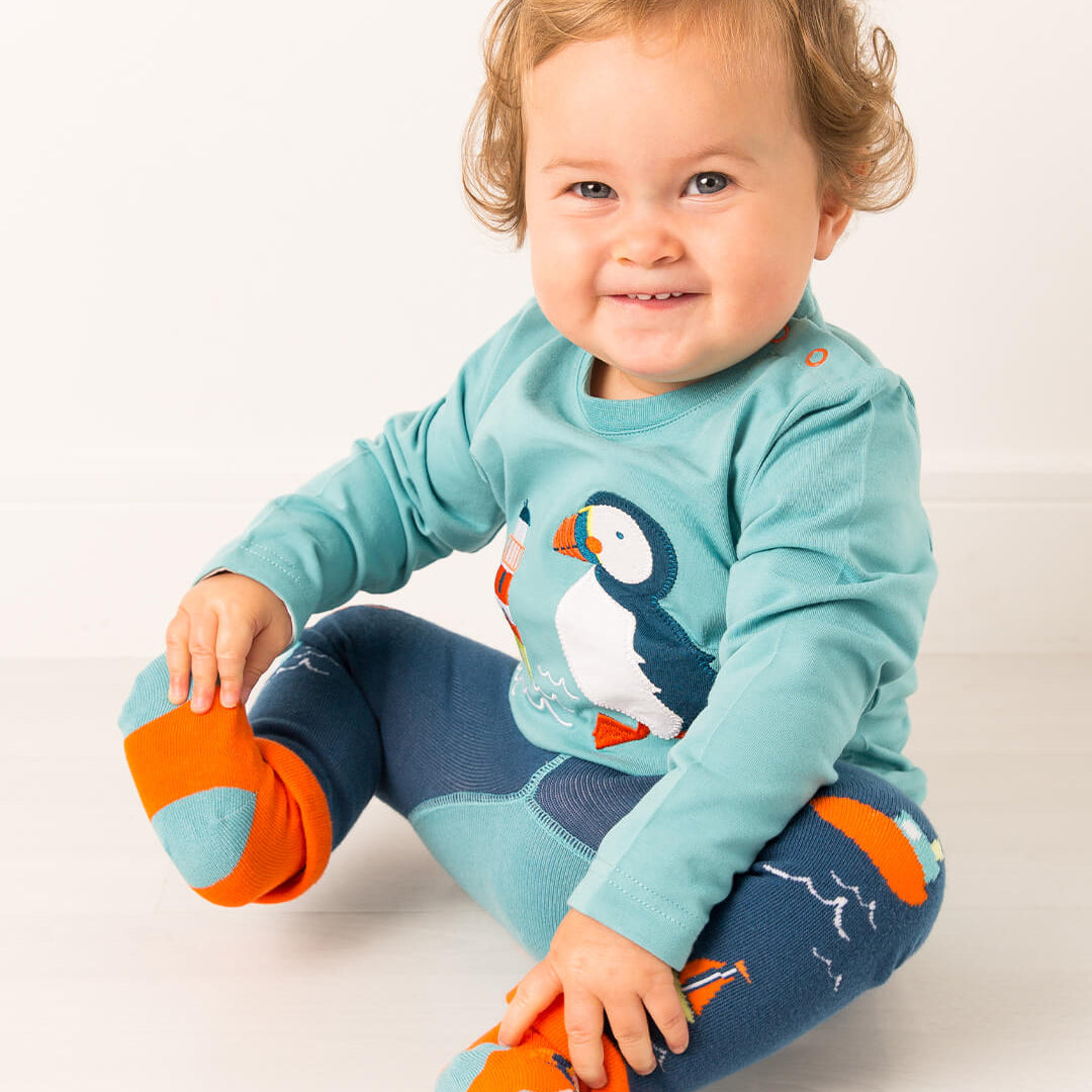Toddler seated wearing the Kenzie the Puffin top, leggings and orange socks