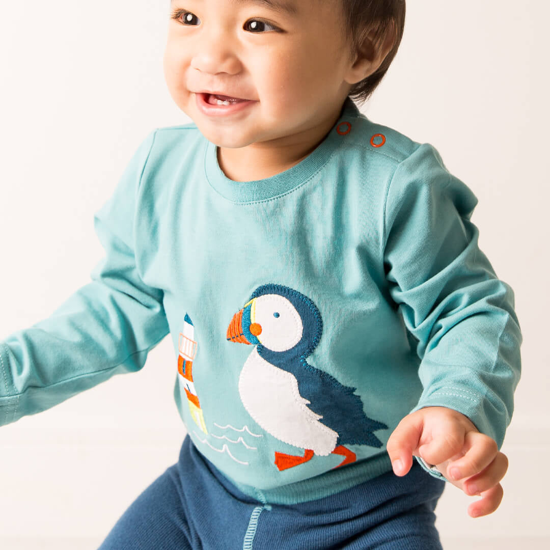 Smiling toddler in the aqua Kenzie the Puffin top with the puffin print visible