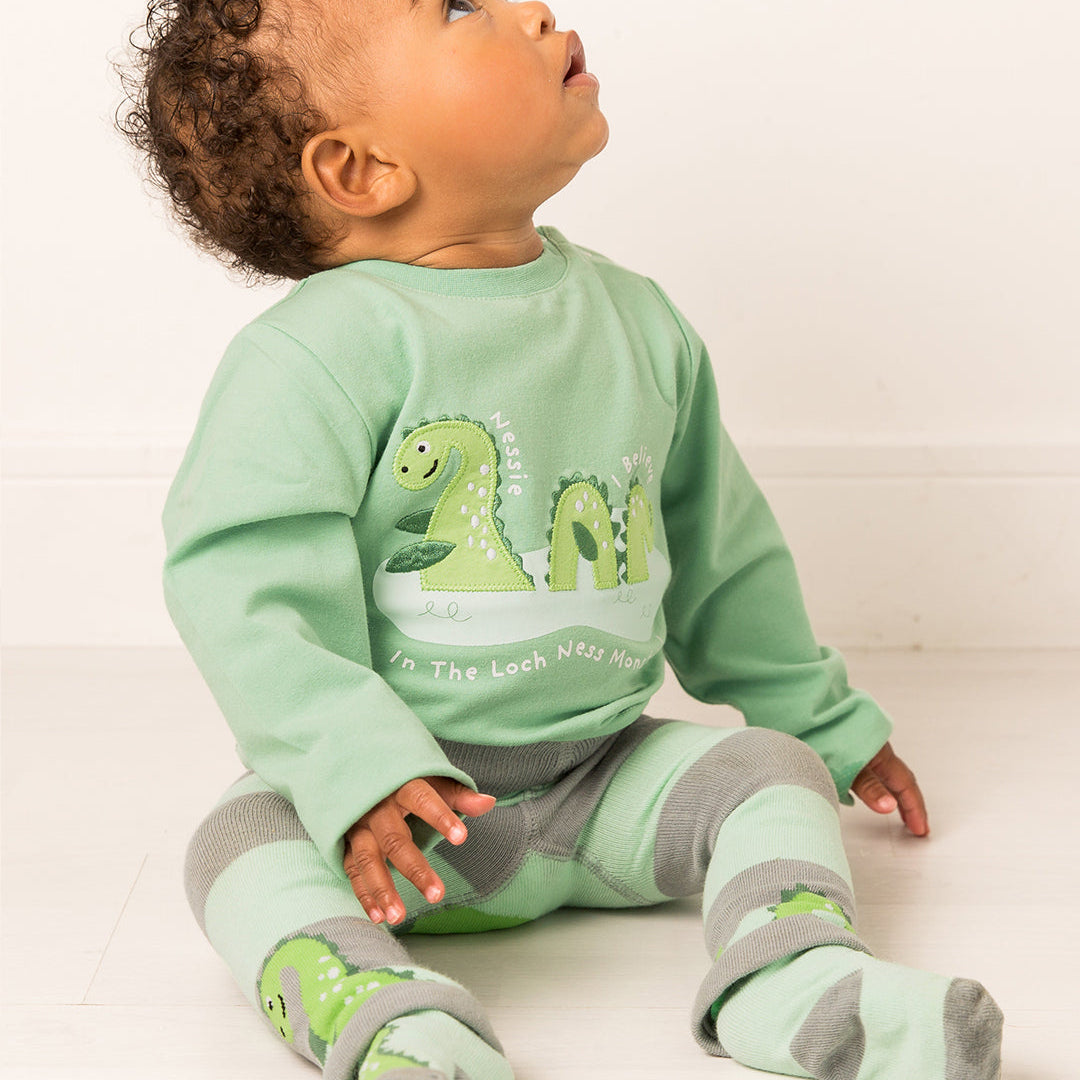 Baby in the green Nessie top looking upwards, seated on a pale floor