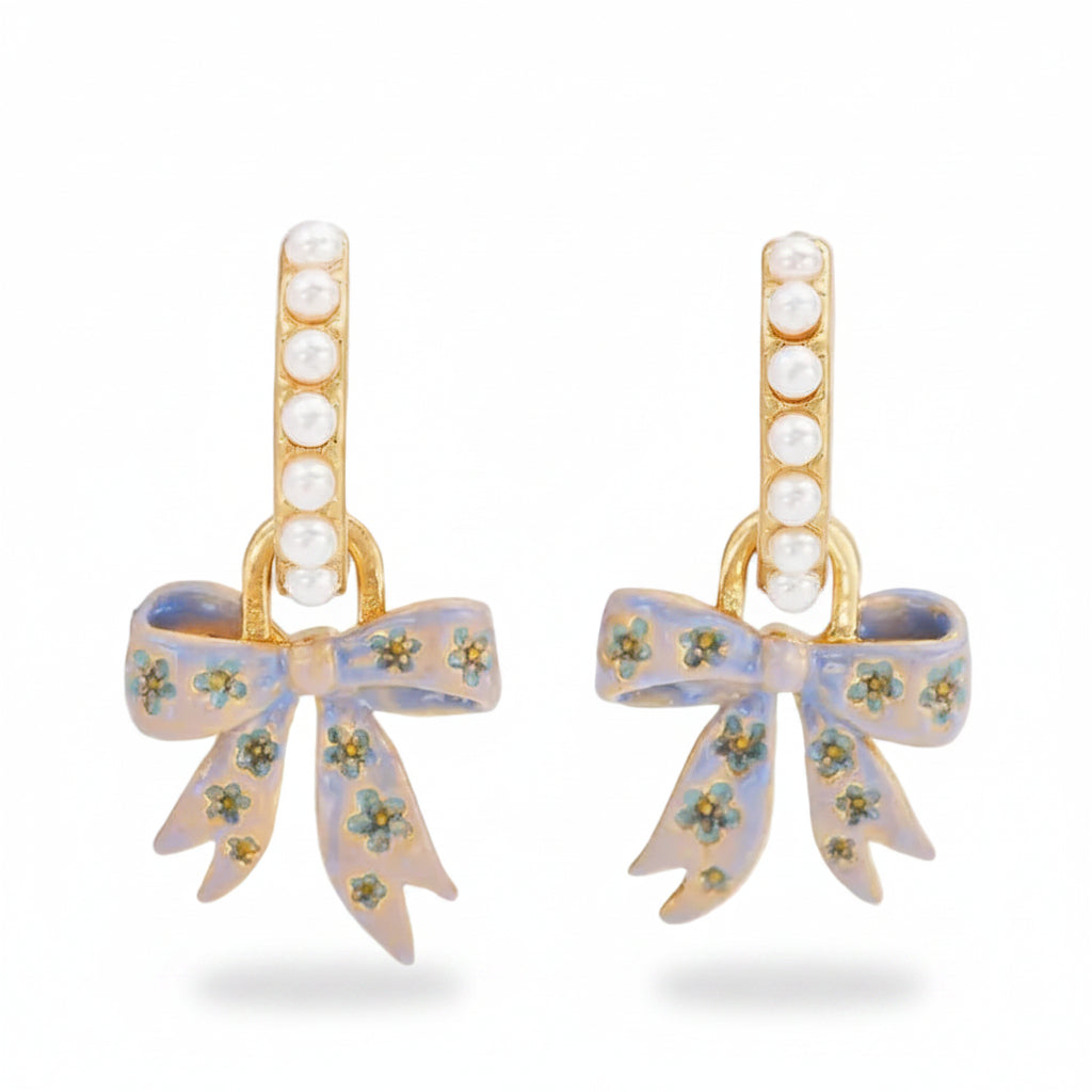 Straight-on view of the earrings showing pearl-set hoops with dangling hand-painted bow charms.