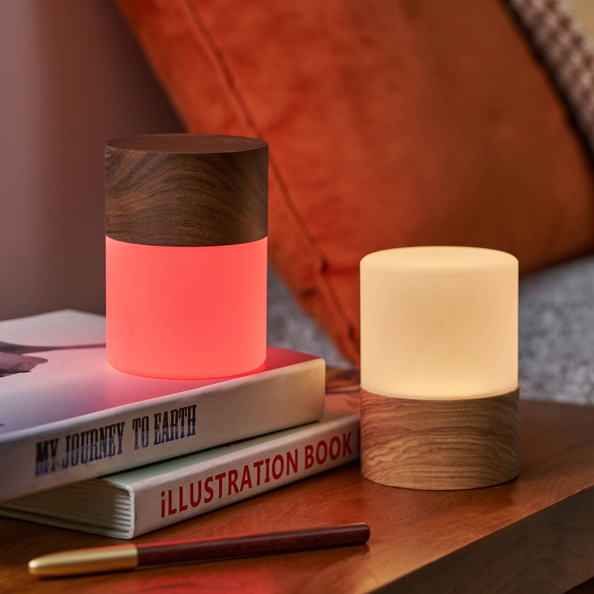 Two Lemelia lights on books beside an orange cushion, pink and warm white