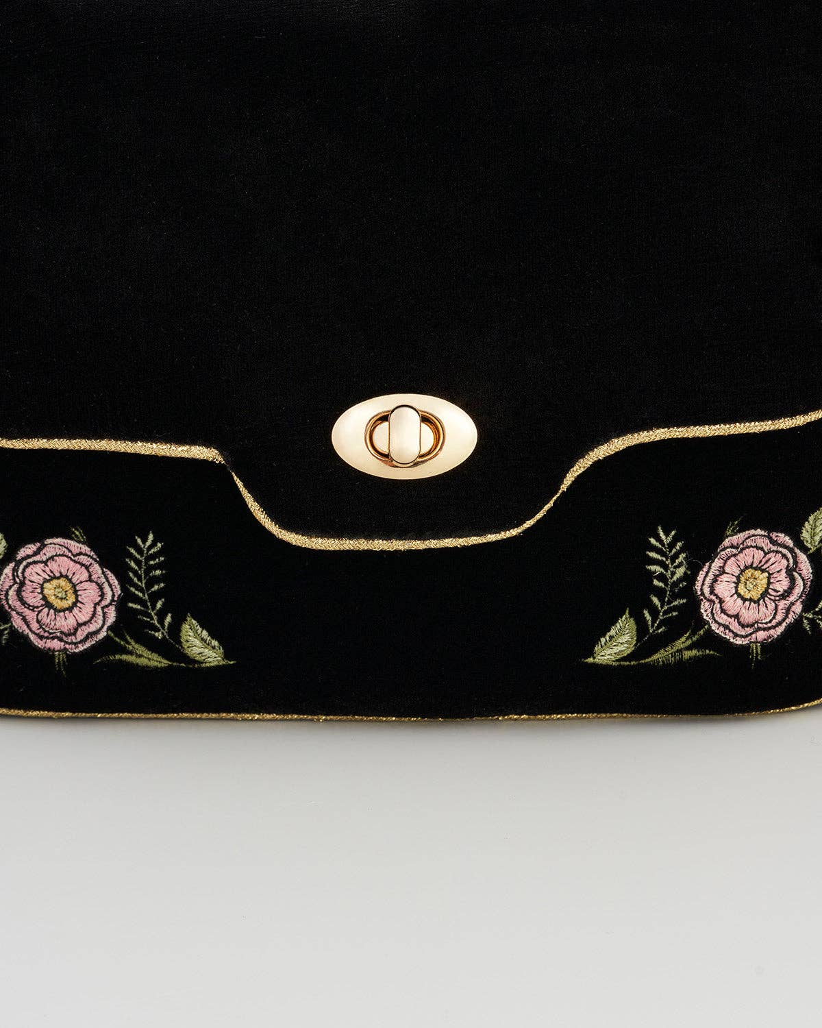 Close-up of gold clasp and rose embroidery on black velvet clutch