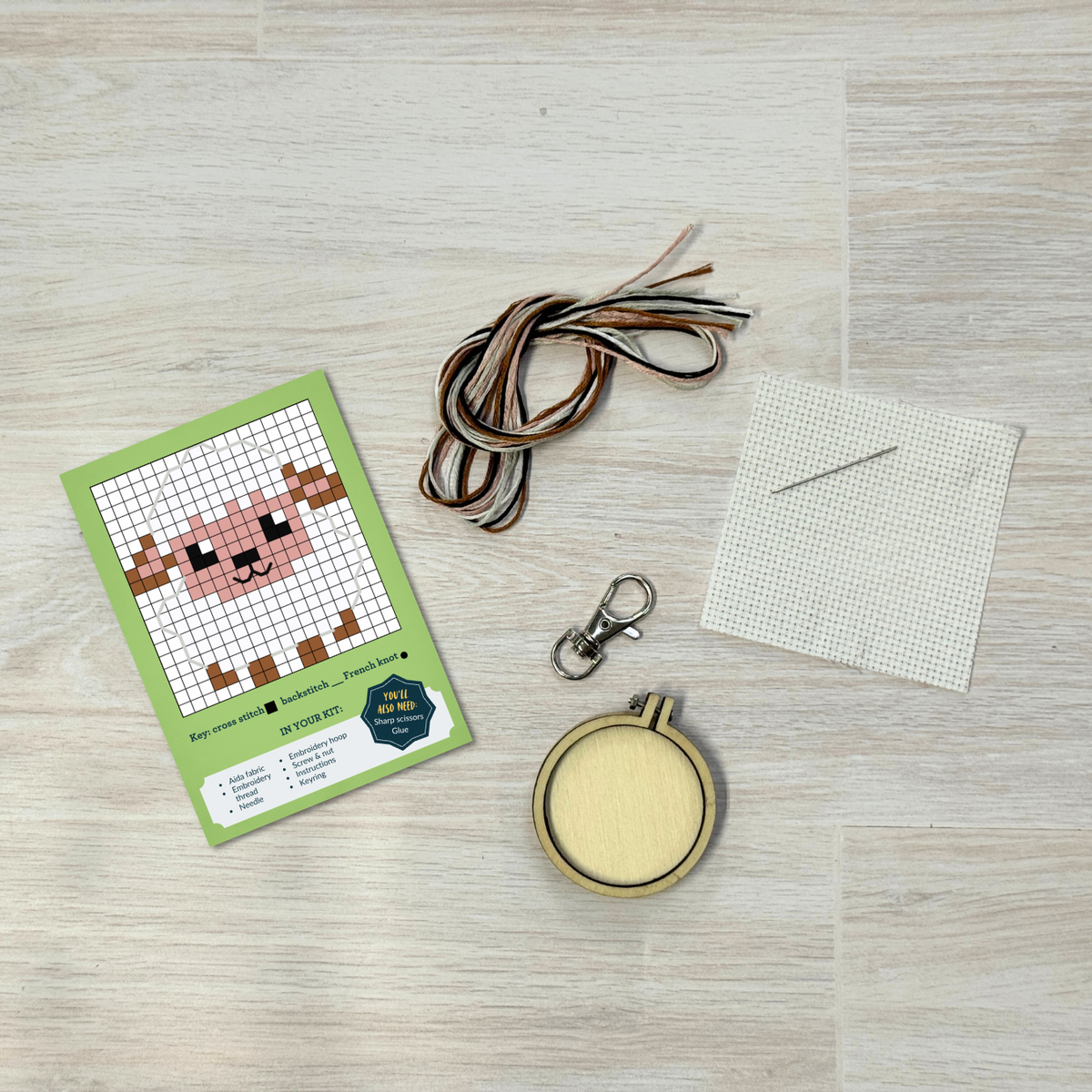 Sheep cross stitch kit contents laid out on pale wood