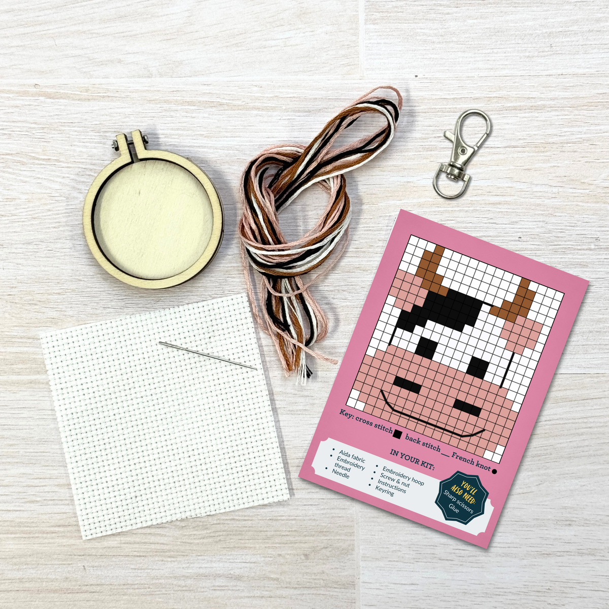 Moody cow cross stitch kit contents laid out on pale wood