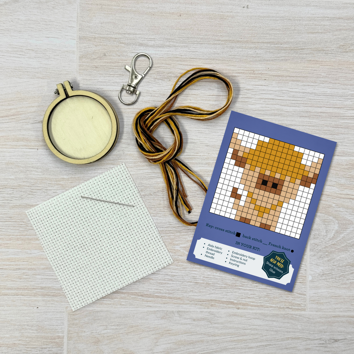 Highland cow cross stitch kit contents laid out on pale wood