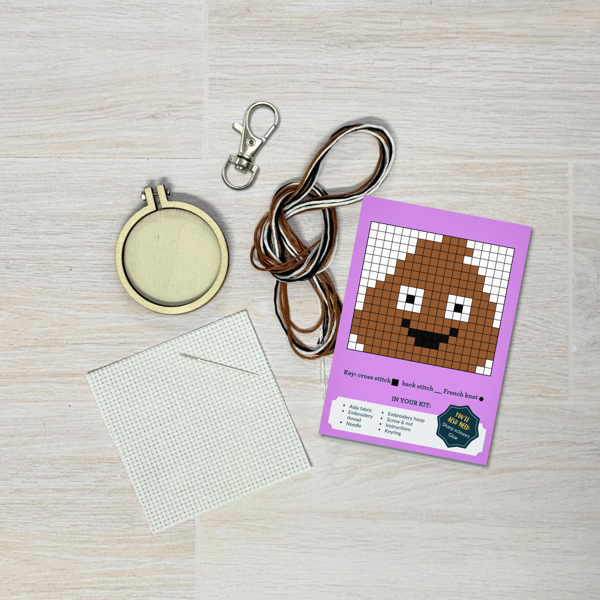 Poo emoji cross stitch kit contents laid out on pale wood