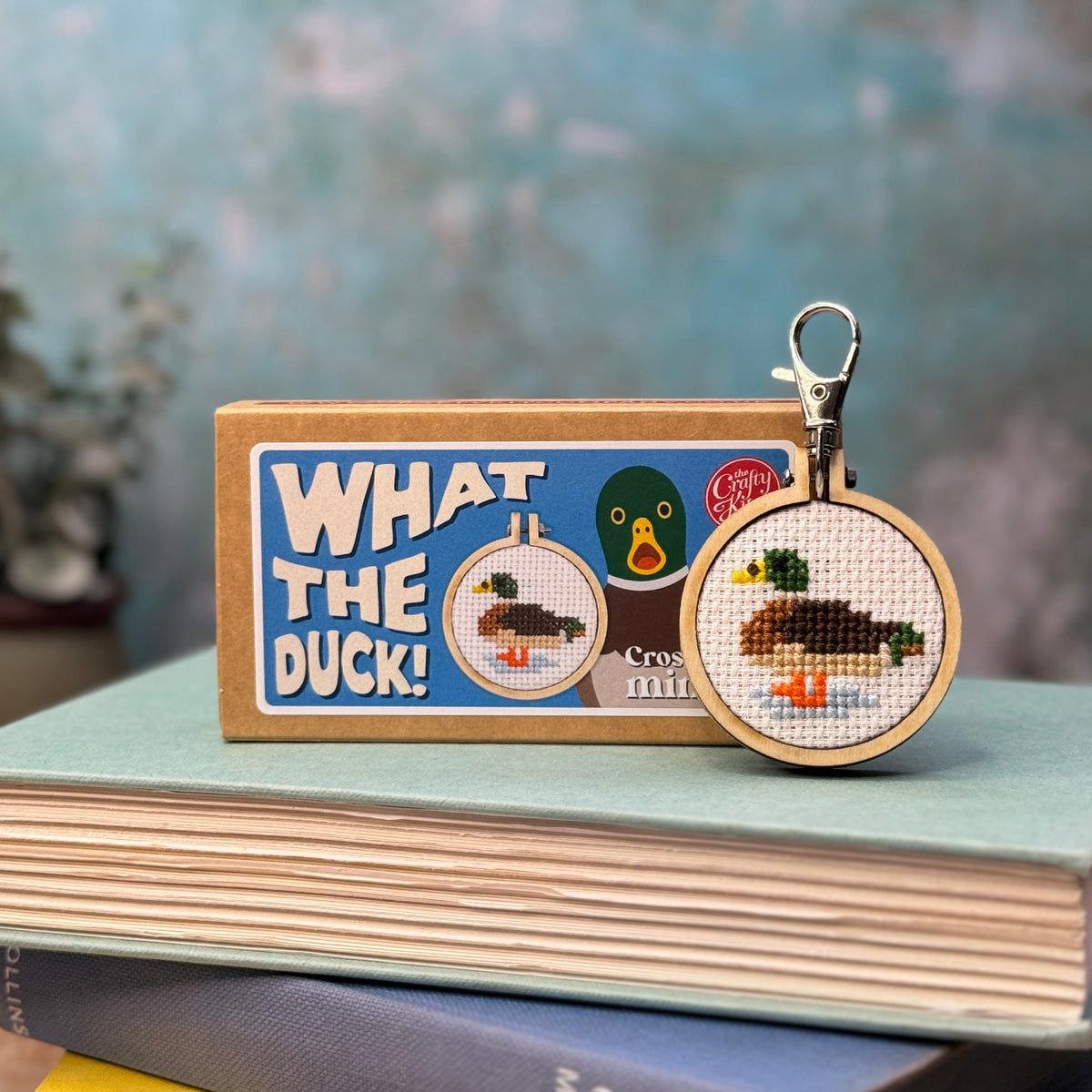 Mallard duck cross stitch keyring and matchbox on a stack of books