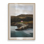 Framed painting of a coastal landscape with a red house on a beige wall.