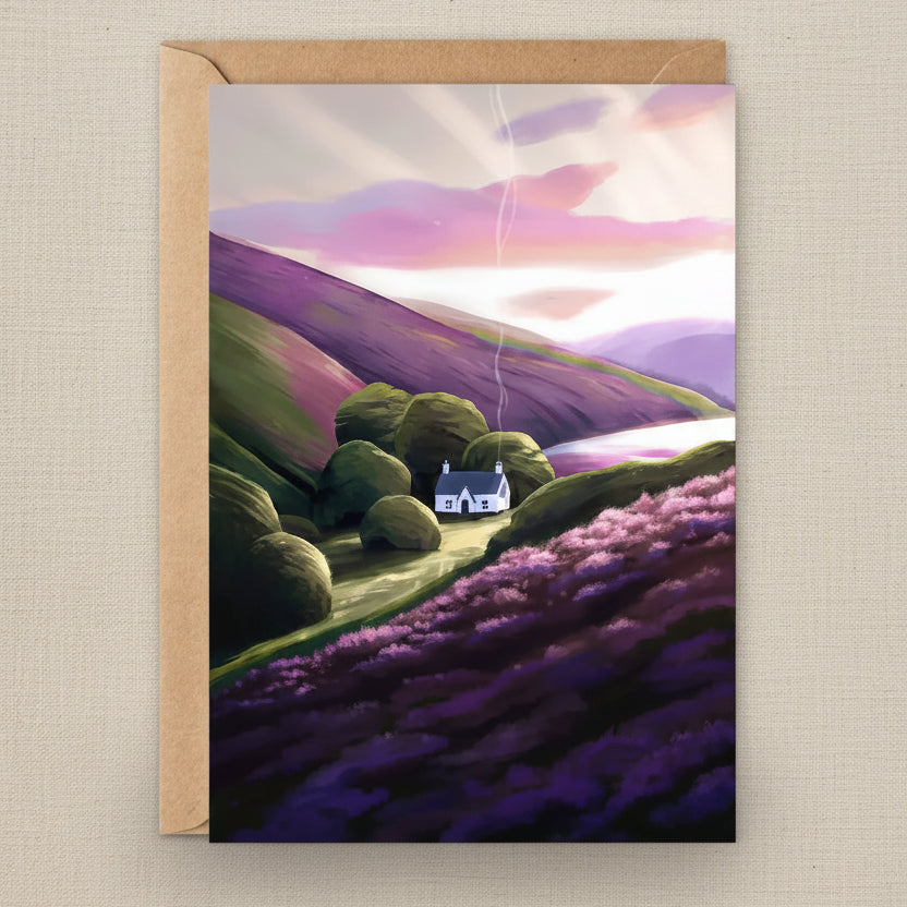 A vertical greeting card with a kraft paper envelope, featuring a stylized landscape illustration of rolling purple and green hills, a small white house, and a pink-lit sky.