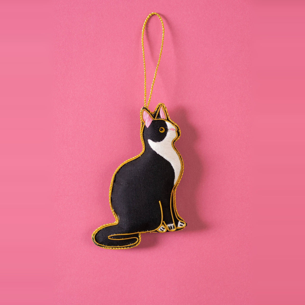 Black and white cat embroidered Christmas decoration with gold outline on a pink background