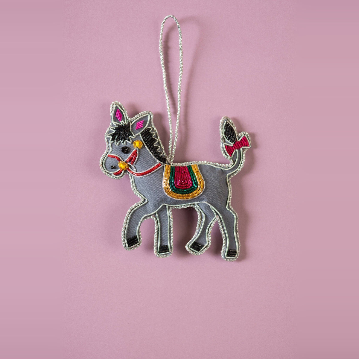 Donkey embroidered Christmas decoration, grey with red bridle and striped saddle, on a mauve background