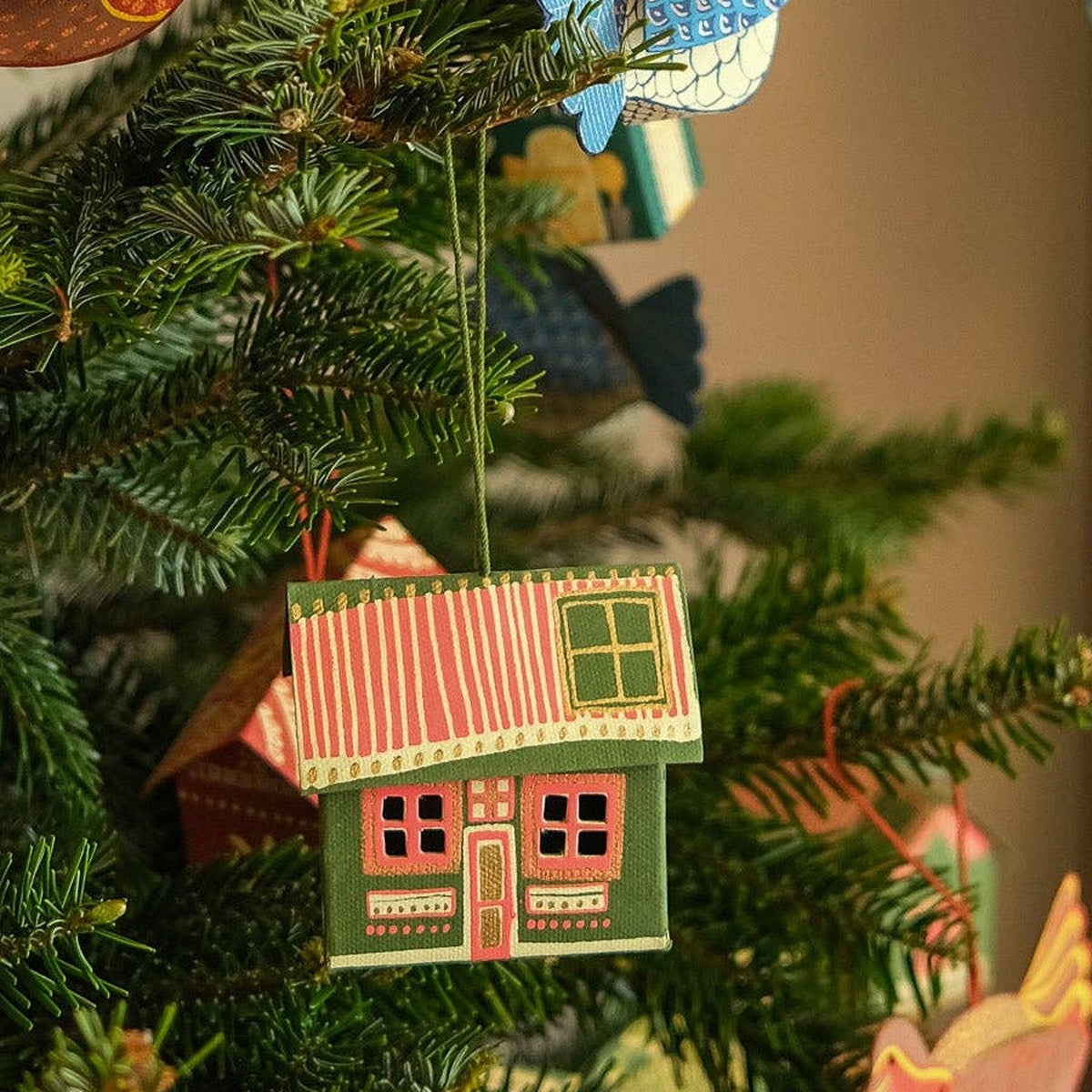 Scottish Bothy board Christmas decoration, green walls and pink roof, hanging on a fir tree