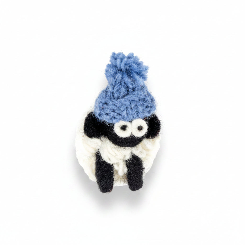 Hand-knitted wool sheep fridge magnet wearing a blue bobble hat
