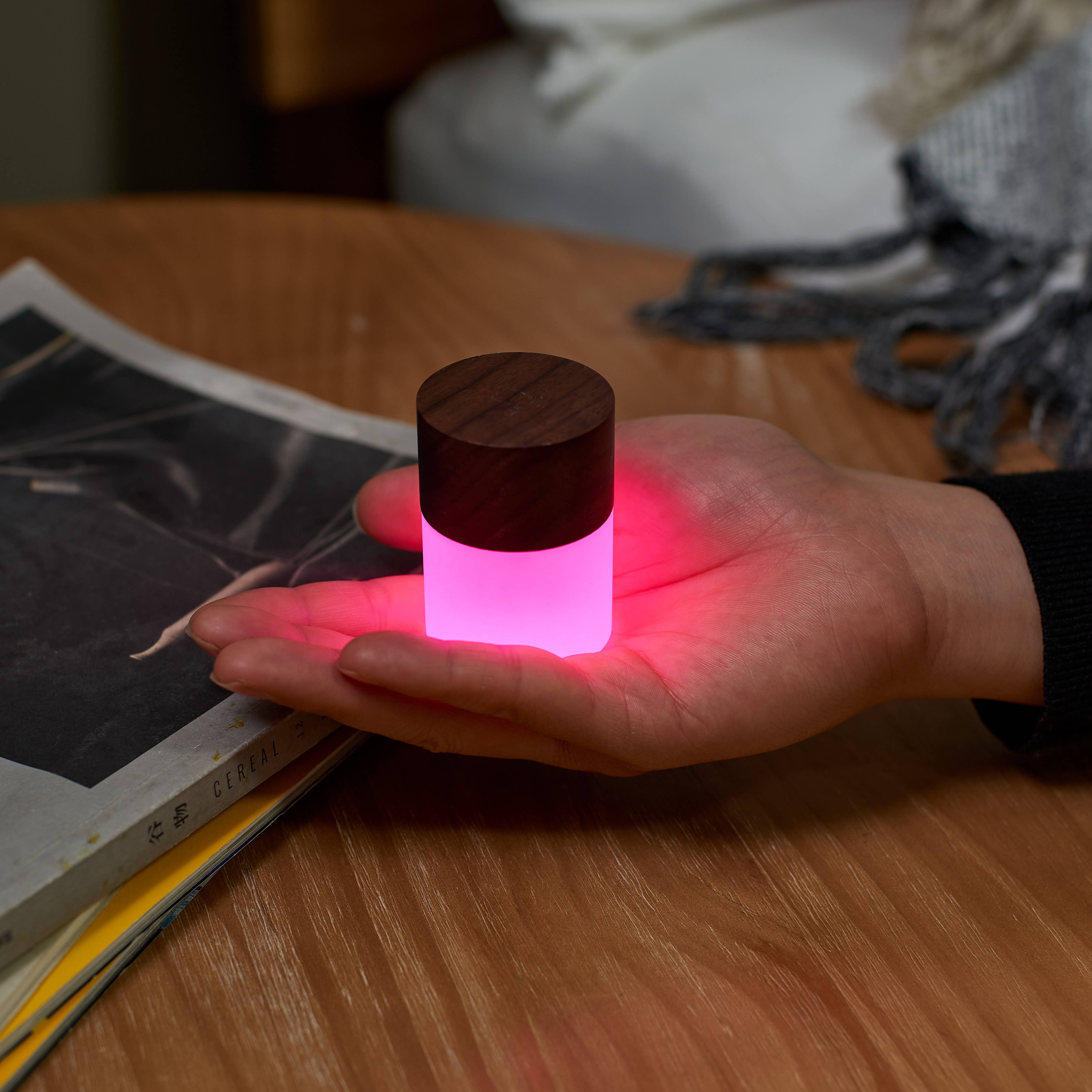 Lemelia mini light with walnut top held in a palm, glowing pink