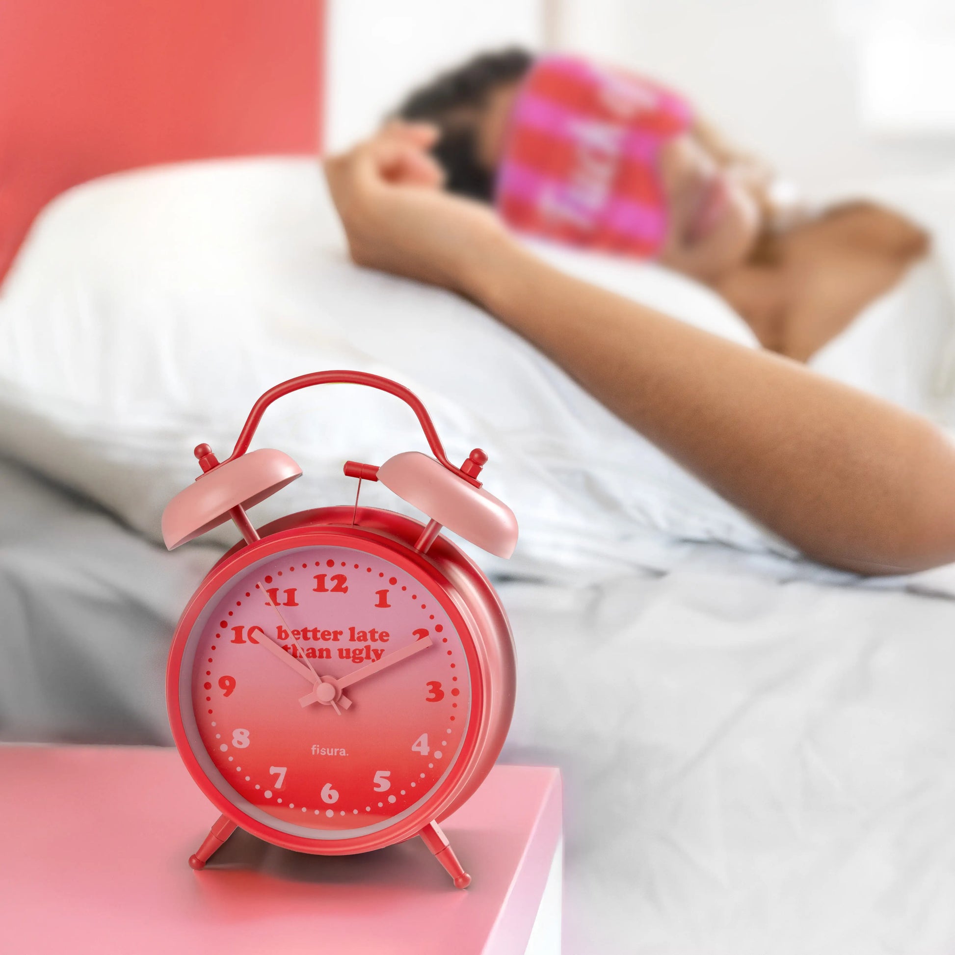 Red alarm clock on a white bedside table beside a pink blanket