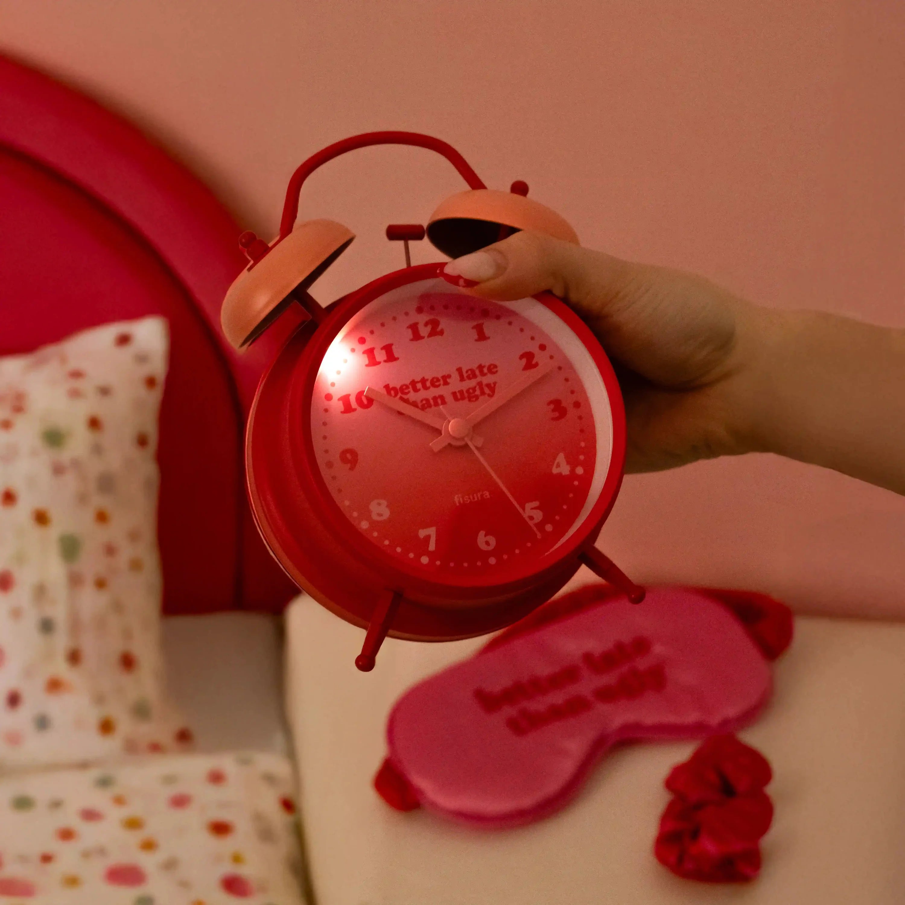 Hand holding the red alarm clock above a spotted duvet