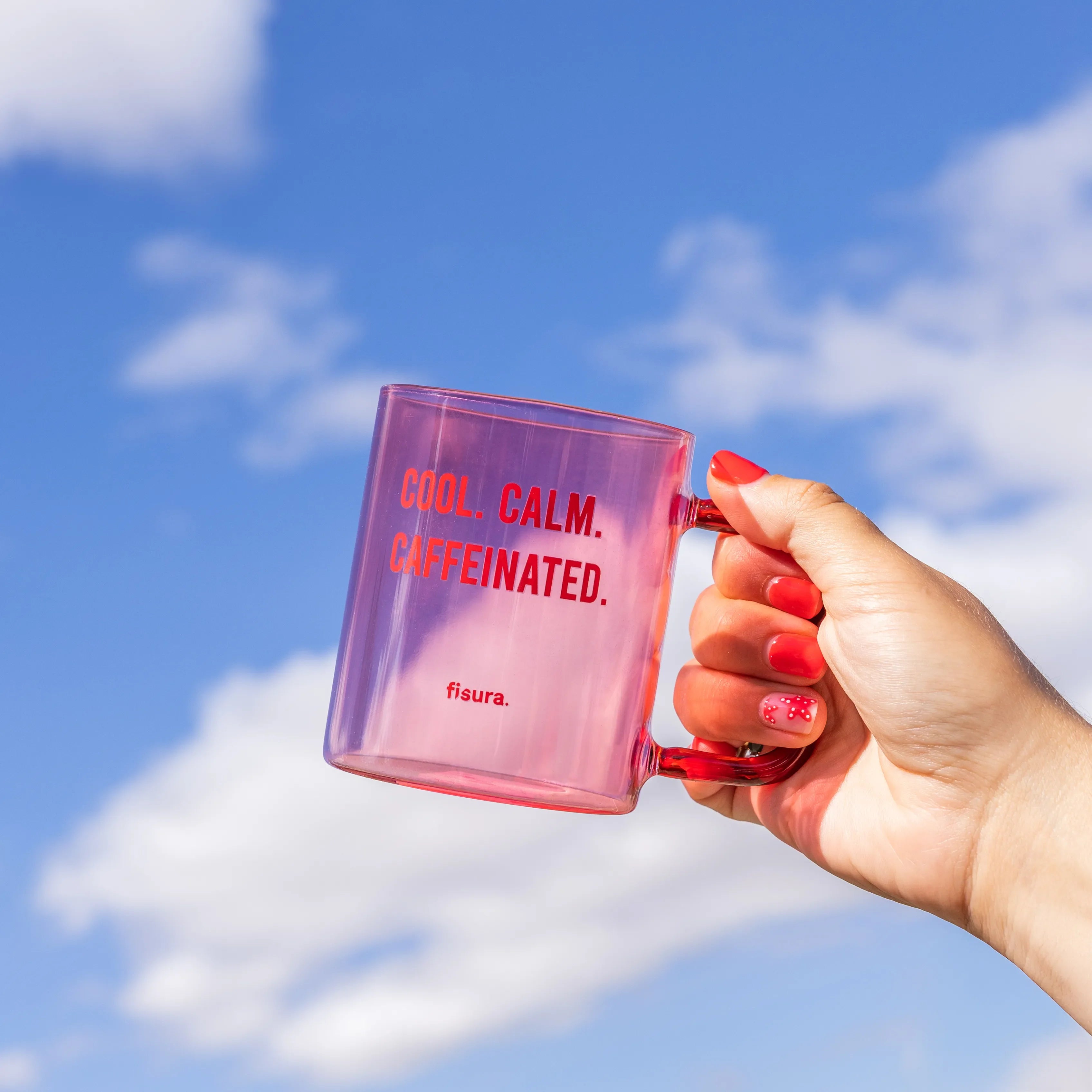 Hand holding the pink glass mug up against a blue sky